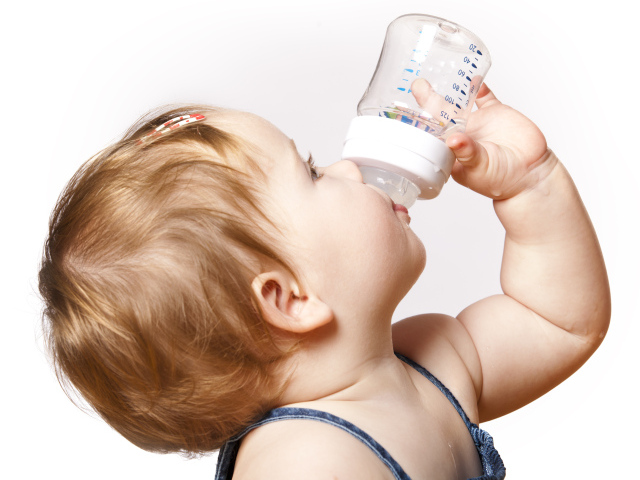 Маленькая девочка пьет молоко с бутылочки на белом фоне