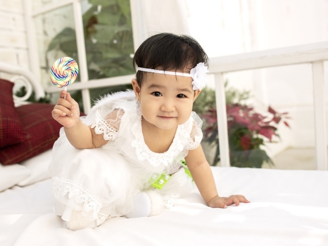 Маленькая девочка в белом платье с леденцом в руке