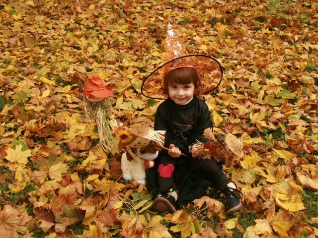 Маленькая девочка в костюме ведьмы сидит на опавшей листве на Хэллоуин