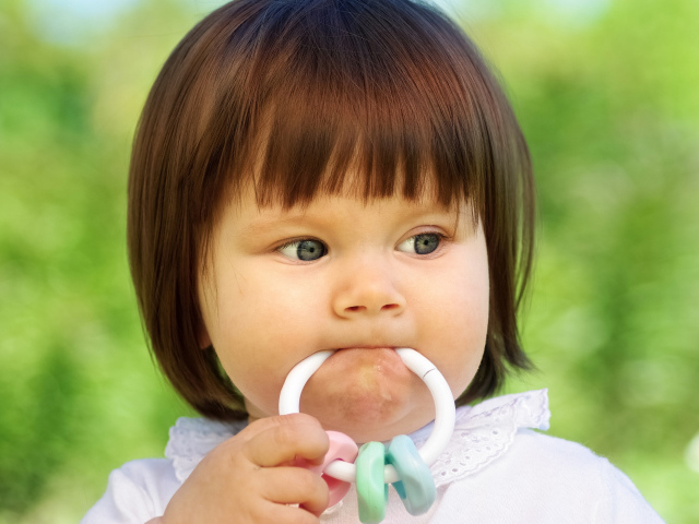 Маленькая девочка с погремушкой во рту