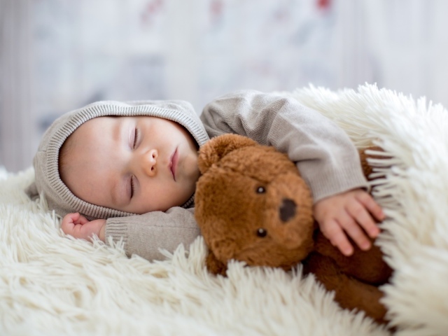 Спящий маленький мальчик обнимает игрушку медвежонка