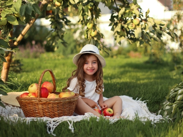 Улыбающаяся девочка сидит на зеленой траве с яблоками