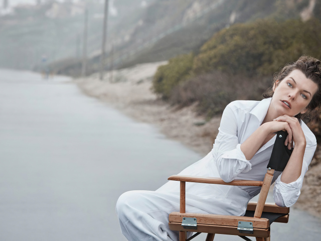 Актриса Милла Йовович в белом платье сидит на стуле