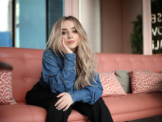 Актриса Сабрина Карпентер сидит на диване в комнате