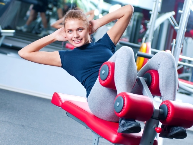 Девушка качает пресс на тренажере в спортзале