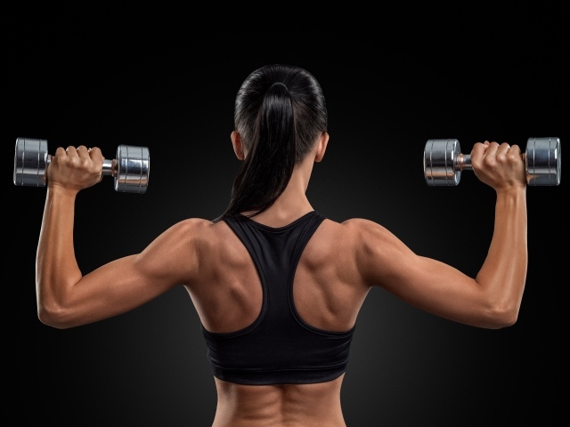 Стройная спортивная девушка с гантелями в руках на черном фоне