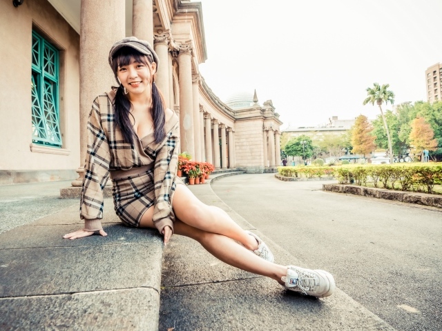Улыбающаяся азиатка в кепке сидит на ступеньках 
