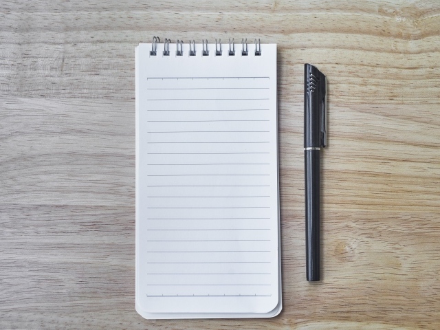 Авторучка и блокнот лежат на деревянном столе