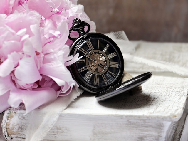 Черные карманные часы с книгой и цветами на столе 