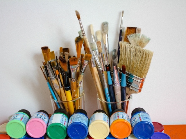 Много кисточек и разноцветные краски у стены