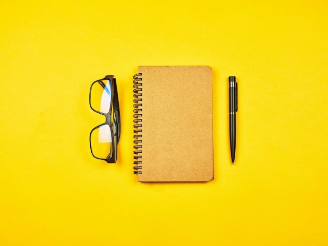 Блокнот, очки и ручка на желтом фоне