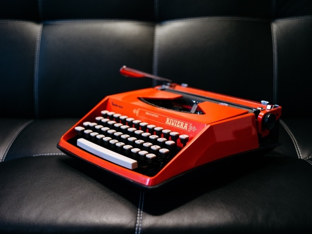 Старая красная печатная машинка на черном диване