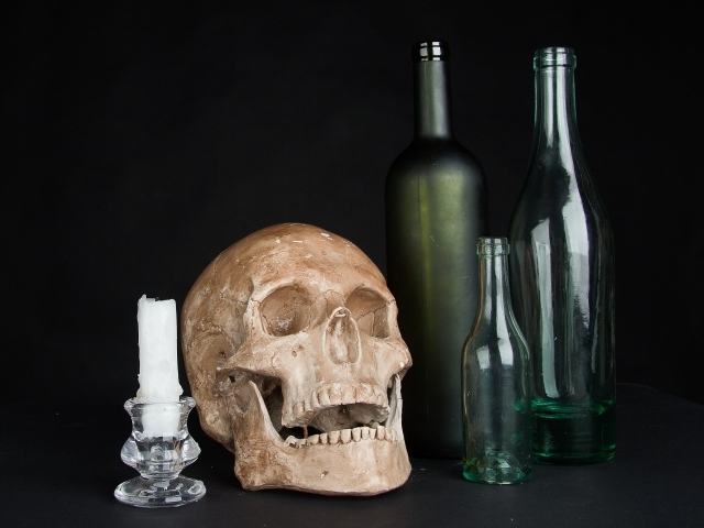 Череп, пустые бутылки и свеча на черном фоне