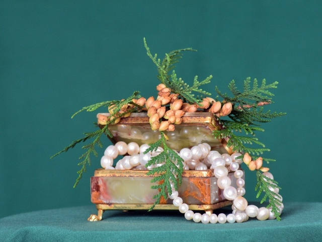 Шкатулка с бусами из жемчуга на зеленом фоне 