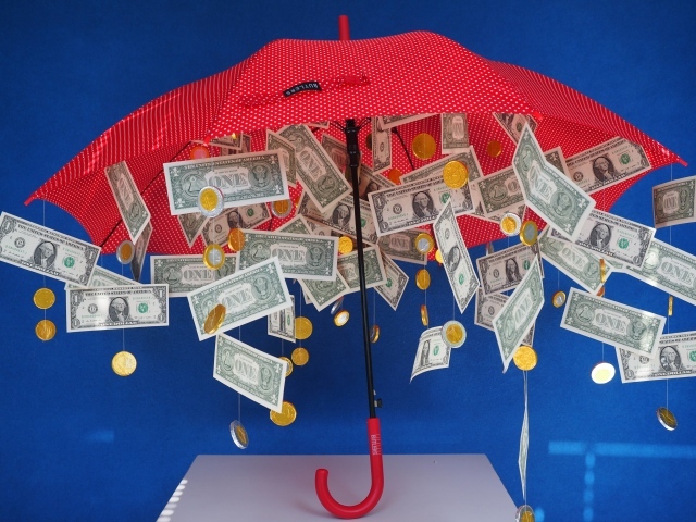 Доллары и монеты высыпаются из зонта на голубом фоне