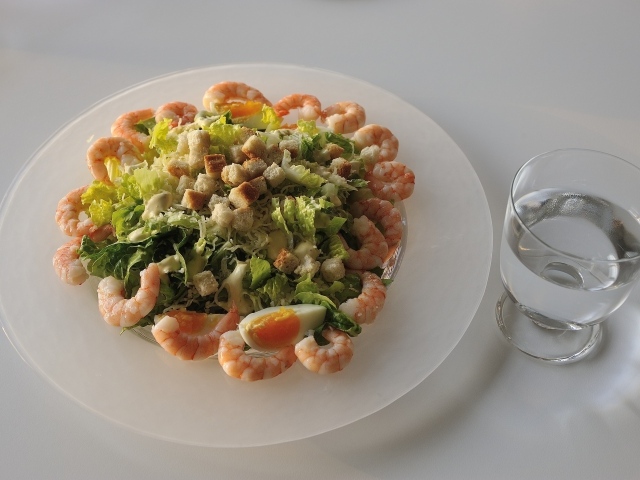 Тарелка аппетитного салата с креветками на столе с рюмкой