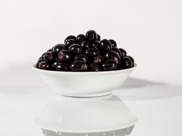 Черные оливки в белой тарелке отражаются в поверхности