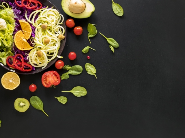 Салат из свежих овощей на черном столе с базиликом, помидорами и авокадо 