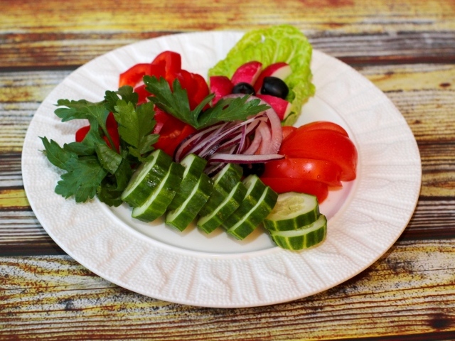 Свежие овощи на белой тарелке на деревянном фоне