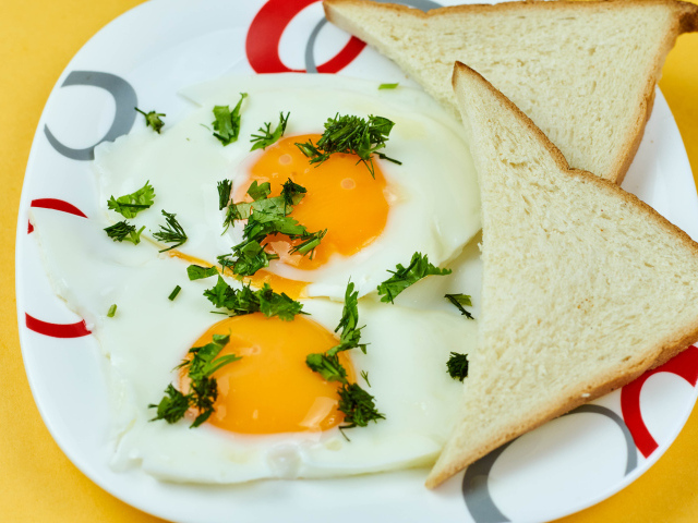 Яичница глазунья с зеленью на тарелке с хлебом 