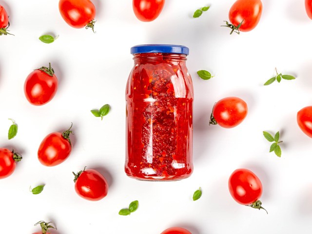 Банка аджики на белом фоне с помидорами