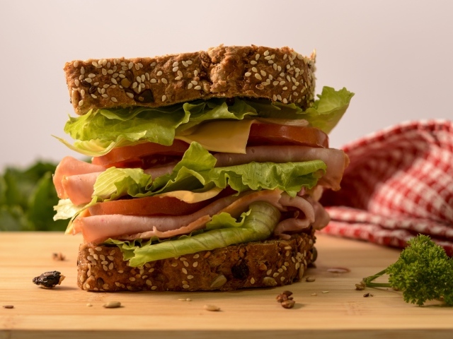 Большой бутерброд с ветчиной, сыром, помидорами и листьями салата 