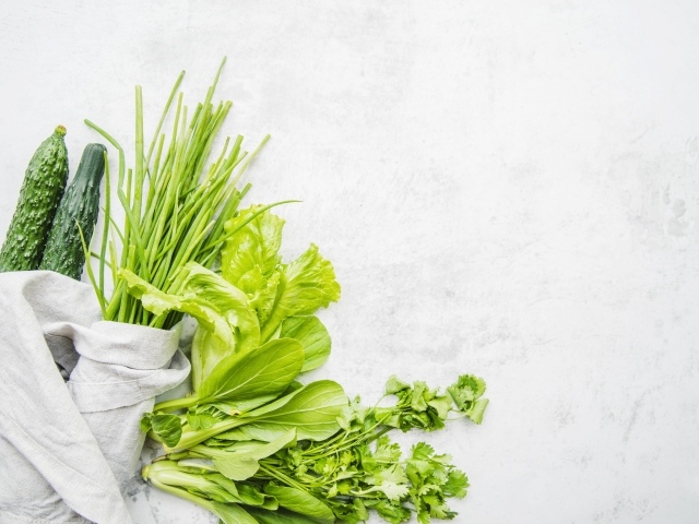 Зелень петрушки и лука, листья салата и свежие огурцы на белом фоне