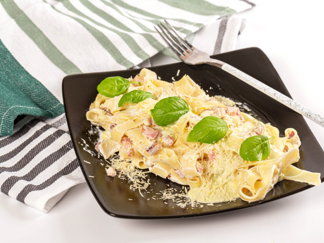 Макароны на тарелке с тертым сыром и кусочками мяса