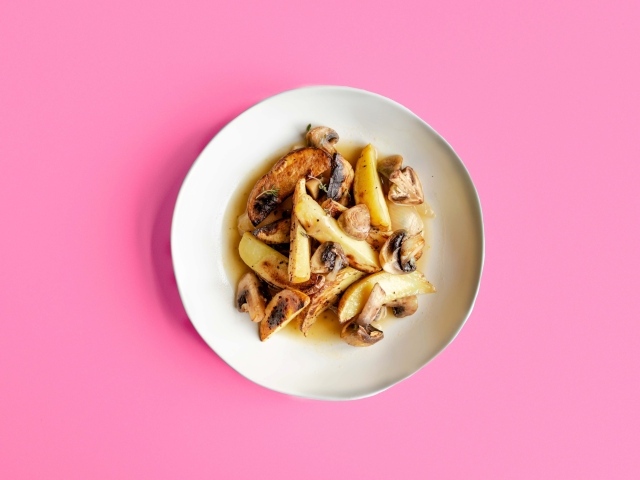 Картофель с грибами в тарелке на розовом фоне 