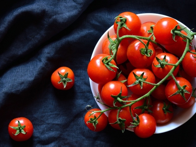 Красные помидоры в белой миске на черном фоне