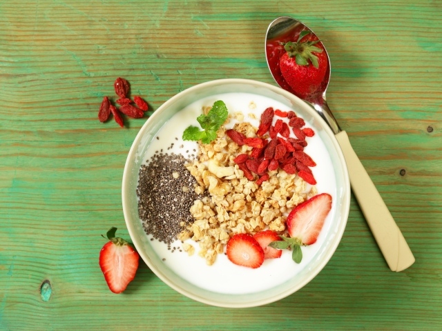 Йогурт с сухофруктами и клубникой на столе в миске 