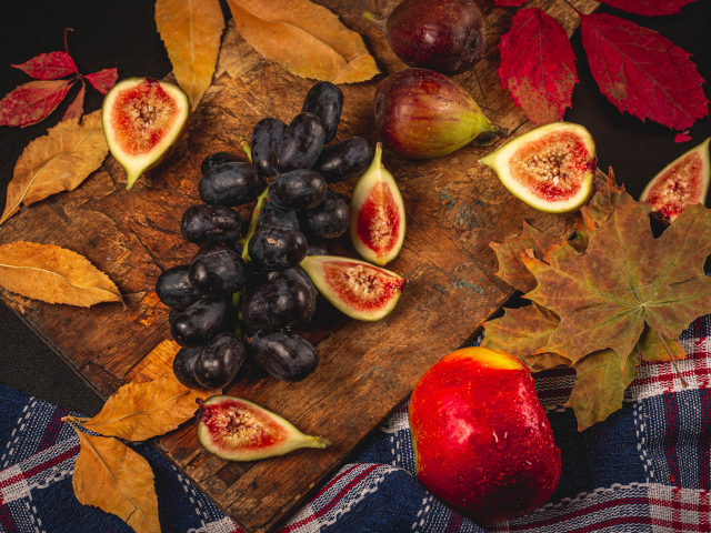 Синий виноград и плоды инжира на столе с листьями