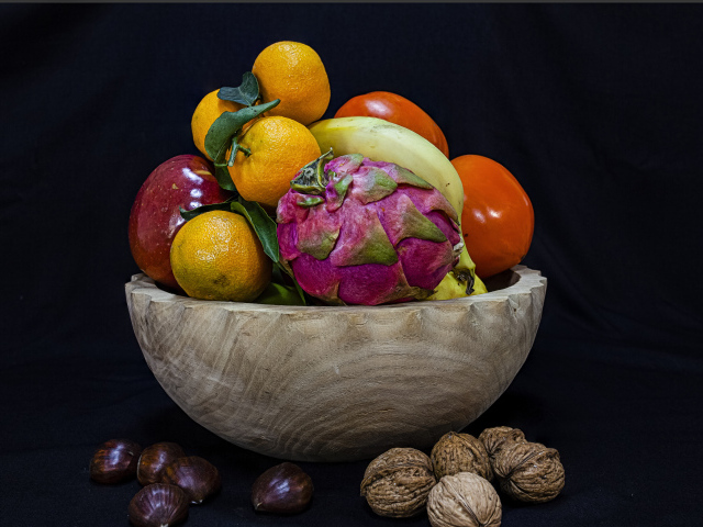 Цитрусовые фрукты в деревянной миске на черном фоне