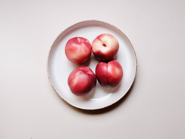 Четыре красных спелых нектарина на тарелке 