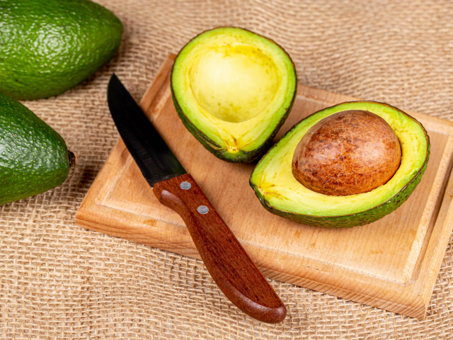 Зеленое авокадо с ножом на разделочной доске