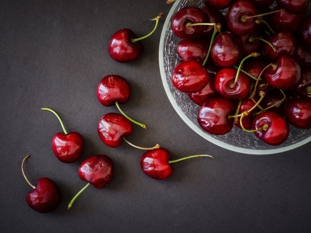 Красные черешни в миске на сером фоне
