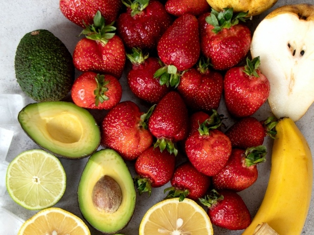 Красная клубника на столе с авокадо, лаймом, грушей и бананом
