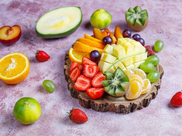 Нарезанные фрукты и ягоды на деревянной доске 