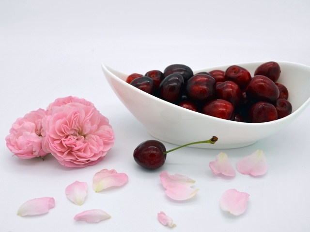 Белая тарелка с красными ягодами черешни на столе с цветами