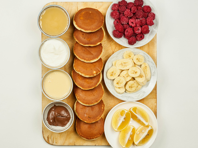 Оладьи с бананами, малиной и апельсином на столе с соусами