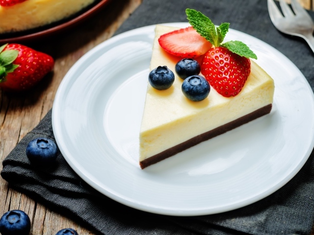 Кусок чизкейка на белой тарелке с клубникой и черникой 