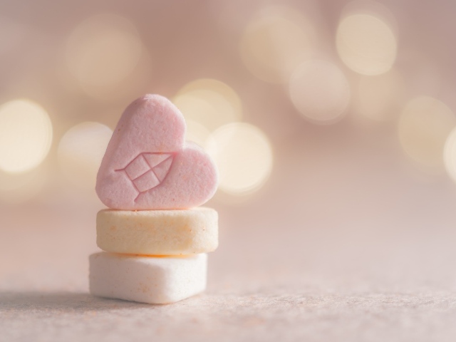 Маленькие конфеты в форме сердца на розовом фоне
