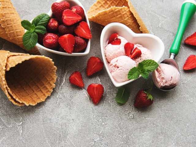 Вафельные рожки на столе с фруктовым мороженым и ягодами клубники 