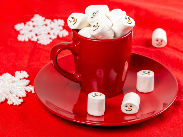 Красная чашка с маршмеллоу на столе со снежинками
