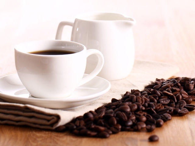 Белая чашка кофе на столе с молоком и зернами