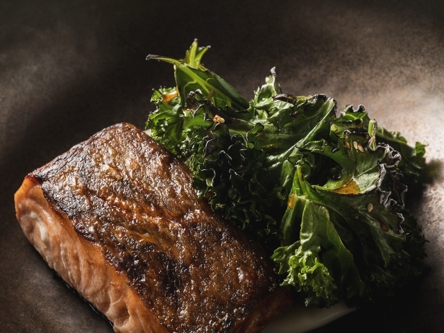 Кусок запеченной рыбы с листьями салата в сковороде 