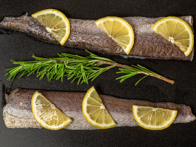 Свежее филе рыбы с лимоном и розмарином на черном фоне