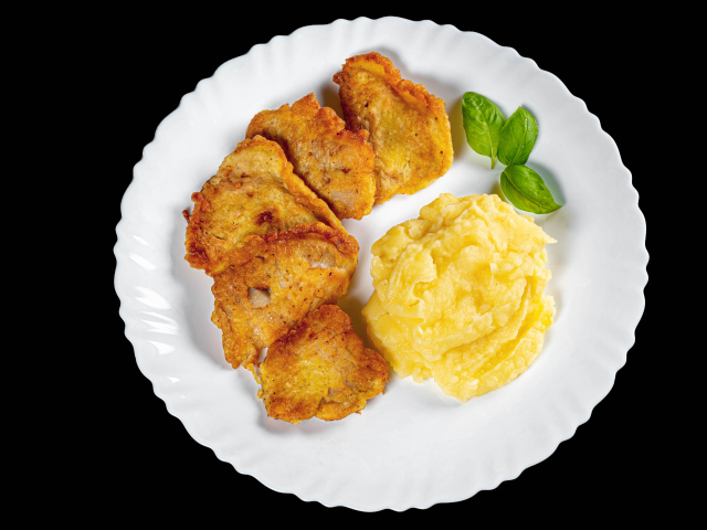 Куски жареной рыбы с картофельным пюре в тарелке на черном фоне