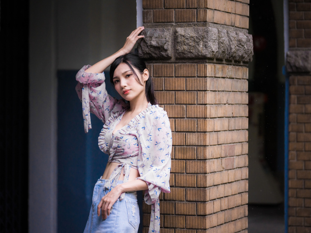 Красивая девушка азиатка стоит у кирпичной колонны 