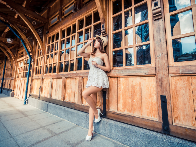 Красивая азиатка в платье стоит у окна кафе